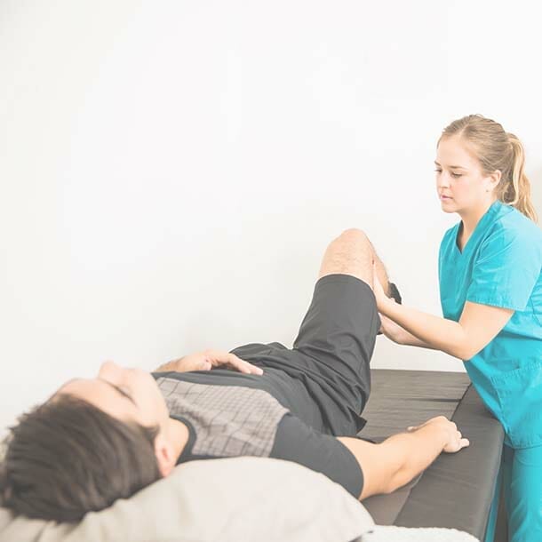Young female physiotherapist helping male athlete with leg exercise in hospital