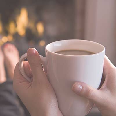 Feet warming at a fireplace with hands holding coffee